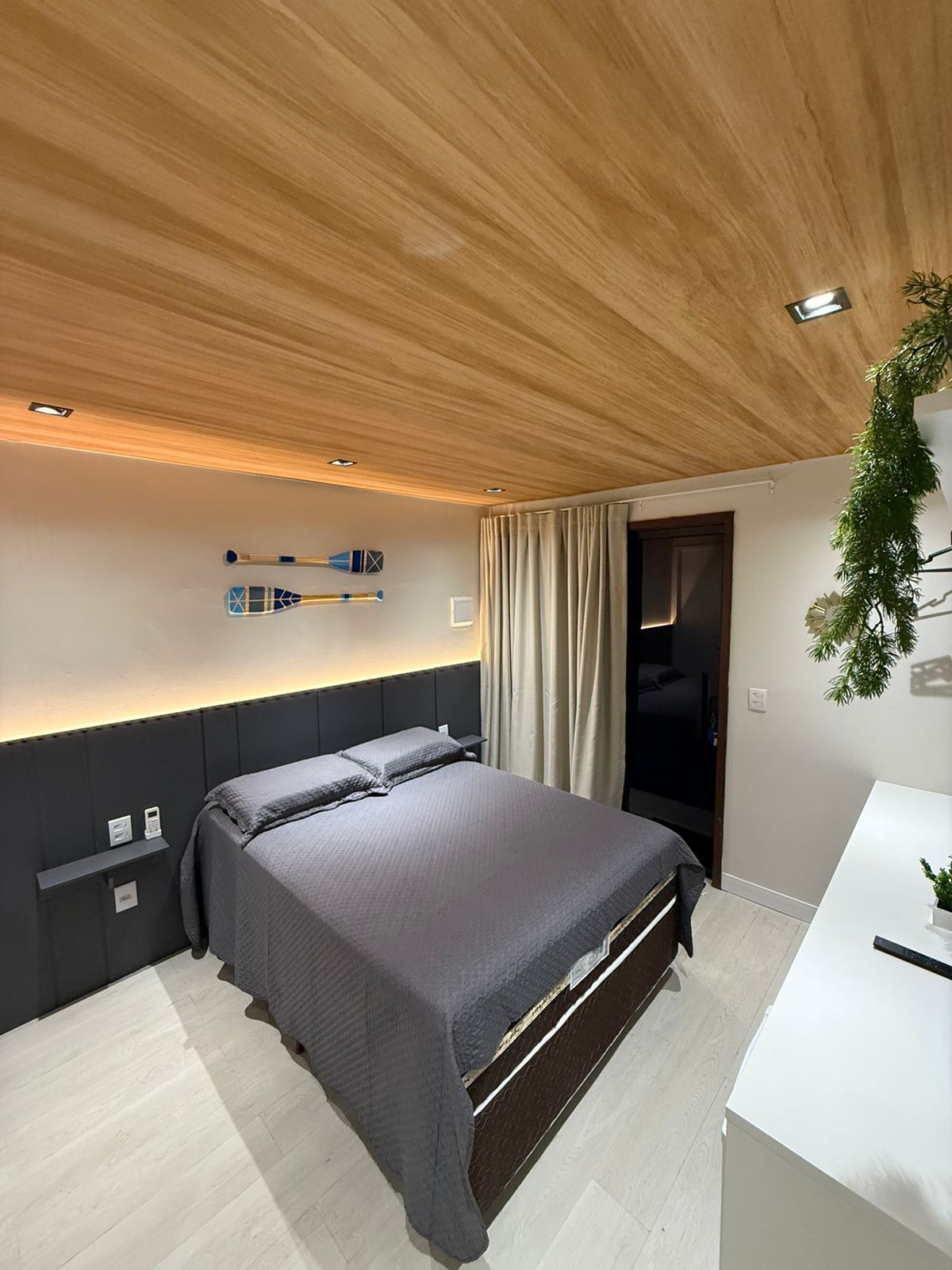 Ein modernes Schlafzimmer mit Holzboden, einem Bett mit grauer Bettwäsche, einem Nachttisch und einem Schreibtisch mit Pflanze.