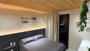 Ein modernes Schlafzimmer mit Holzboden, einem Bett mit grauer Bettwäsche, einem Nachttisch und einem Schreibtisch mit Pflanze.
