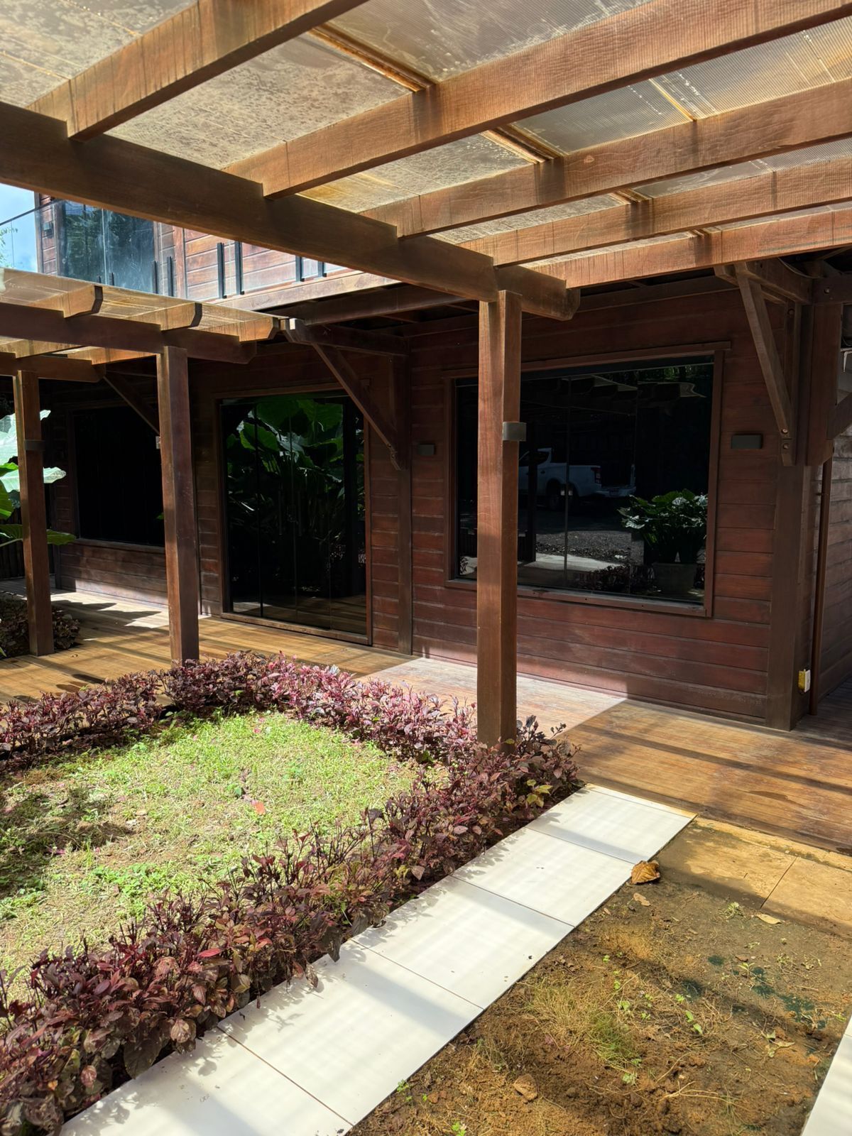 A covered outdoor area with a wooden pergola, a paved walkway, and a landscaped garden with various plants.