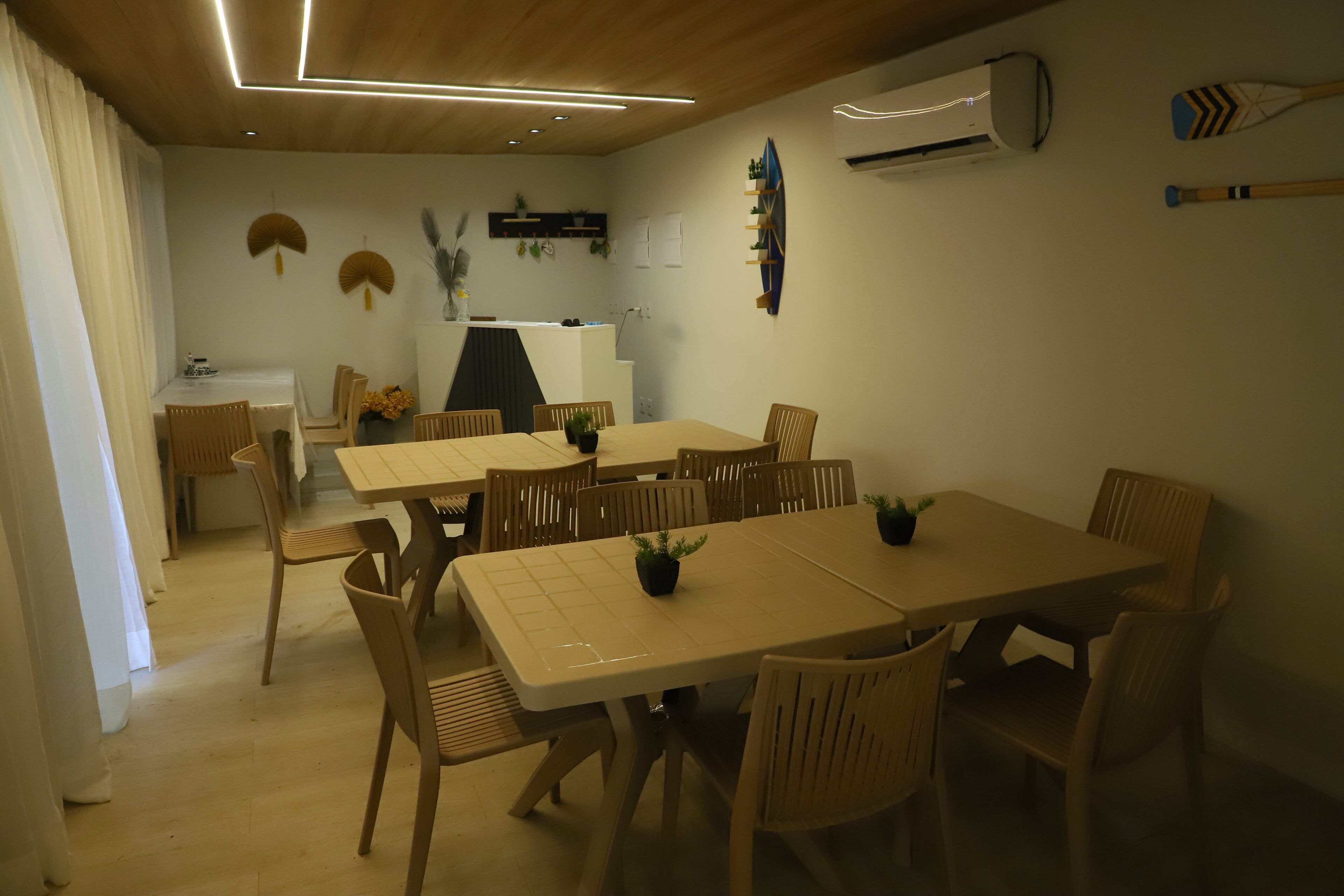 A dining area with a long table and chairs, a kitchen area with a counter, and an air conditioning unit on the wall.