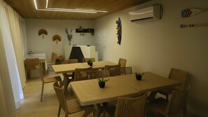 Un comedor con una mesa larga y sillas, una zona de cocina con mostrador y un equipo de aire acondicionado en la pared.