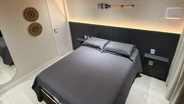 Un dormitorio moderno con una cama grande, cabecera, mesita de noche, espejo y elementos decorativos en la pared.