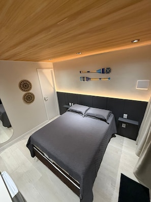Un dormitorio moderno con una cama grande, cabecera, mesita de noche, espejo y elementos decorativos en la pared.