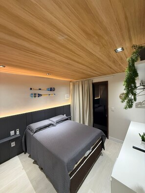 Un dormitorio moderno con techo de madera, una cama con ropa de cama gris, una mesita de noche y una pequeña planta.