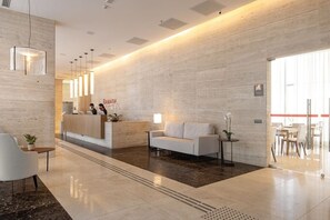 A modern reception area with a marble floor, a reception desk, a sofa, and a potted plant. - Flat Particular no Hotel Ramada Brasília (Brasília)