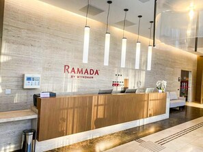 A reception desk with a wooden finish, a wall-mounted control panel, and pendant lighting.