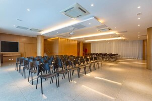 Un salón de conferencias con filas de sillas, un proyector y una pantalla.