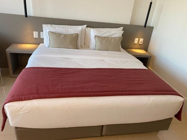 A modern hotel room with a large bed, two bedside tables, and a headboard.