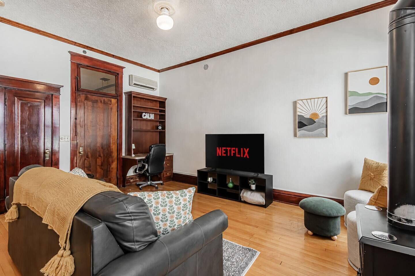 Ein Wohnzimmer mit einer Ledersofa, einem Fernseher, der 'NETFLIX' anzeigt, einem Holzschrank und einem Kamin.