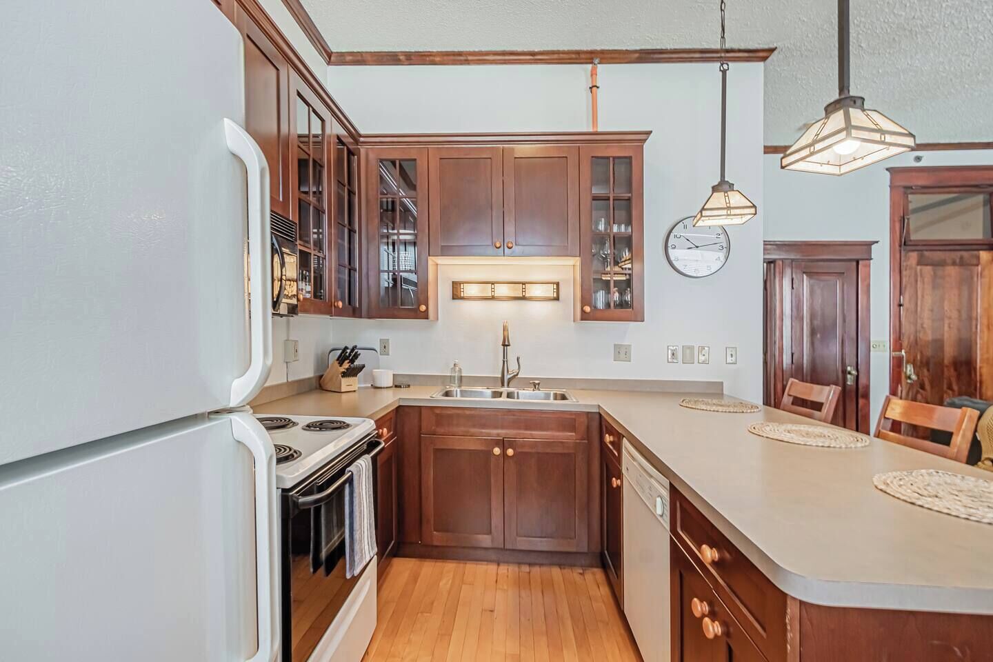 A kitchen with wooden cabinets, a built-in oven, a sink, and pendant lighting.