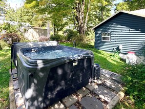 Un bain à remous dans un jardin, avec un chalet en bois en arrière-plan.