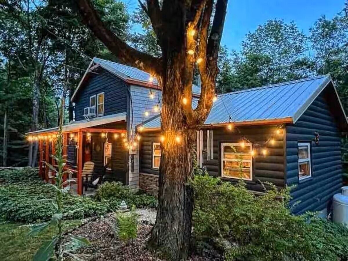 A cabin with a porch and string lights, surrounded by trees.