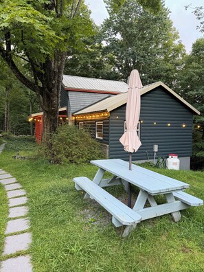 A wooden cabin with a picnic table and umbrella, surrounded by lush greenery and a stone pathway. - The Beech Street Bungalow-  Hottub + Pedal Boat (Smallwood)