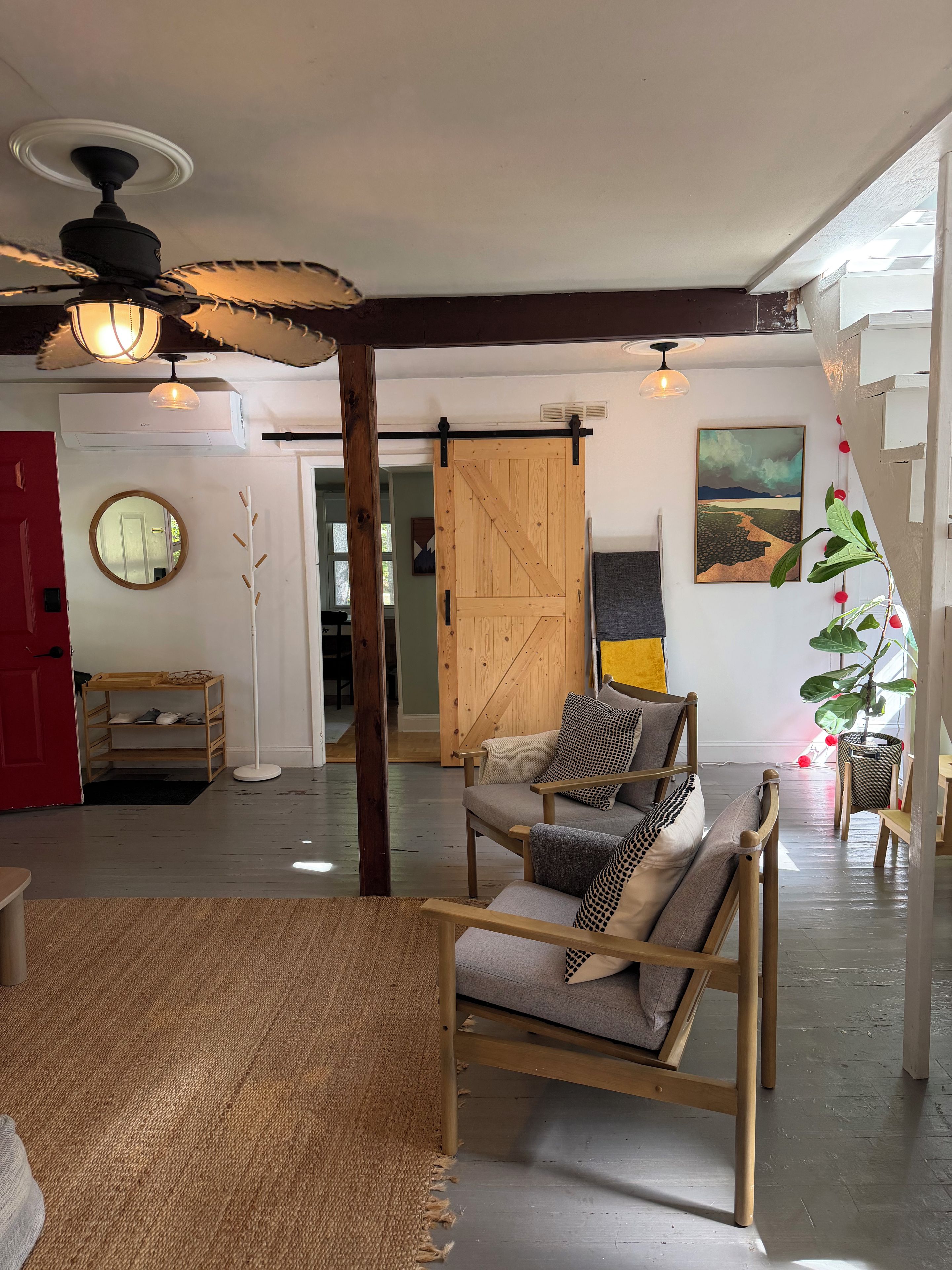 A spacious living area with a wooden sofa, a ceiling fan, a large mirror, and a sliding barn door.