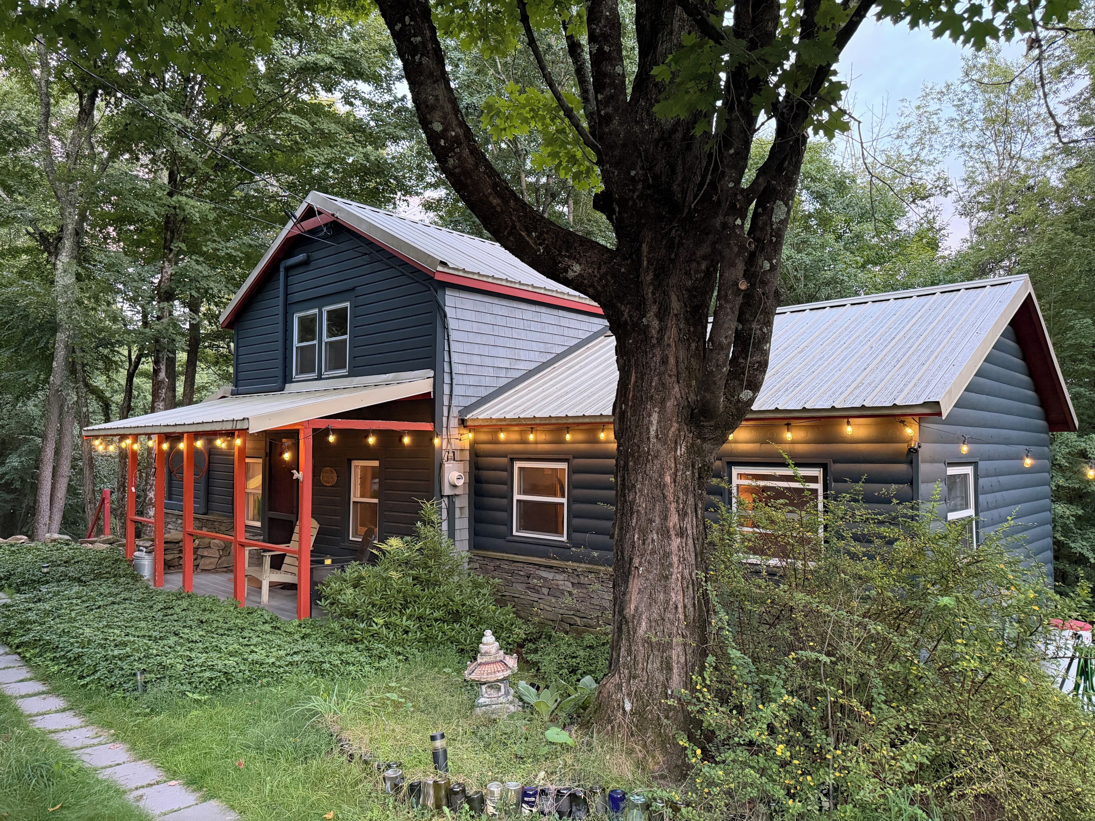 A cabin with a porch, surrounded by trees and a garden.