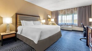 Una camera d'albergo con un letto grande, due lampade ai lati del letto, una scrivania con una sedia e una finestra con tende.