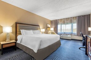 Habitación de hotel con una cama grande, dos lámparas de noche, un escritorio con silla y una ventana con cortinas.