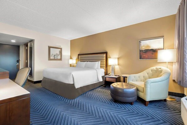 Una habitación de hotel con cama, una silla, un escritorio y una lámpara.