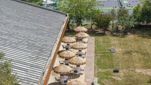 Un edificio con tetto spiovente, posti a sedere all'aperto con ombrelloni e una zona verde con alberi.