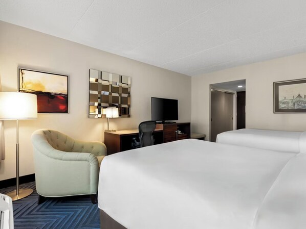 Una habitación de hotel con una cama, un escritorio, una silla, un televisor y un cuadro en la pared.