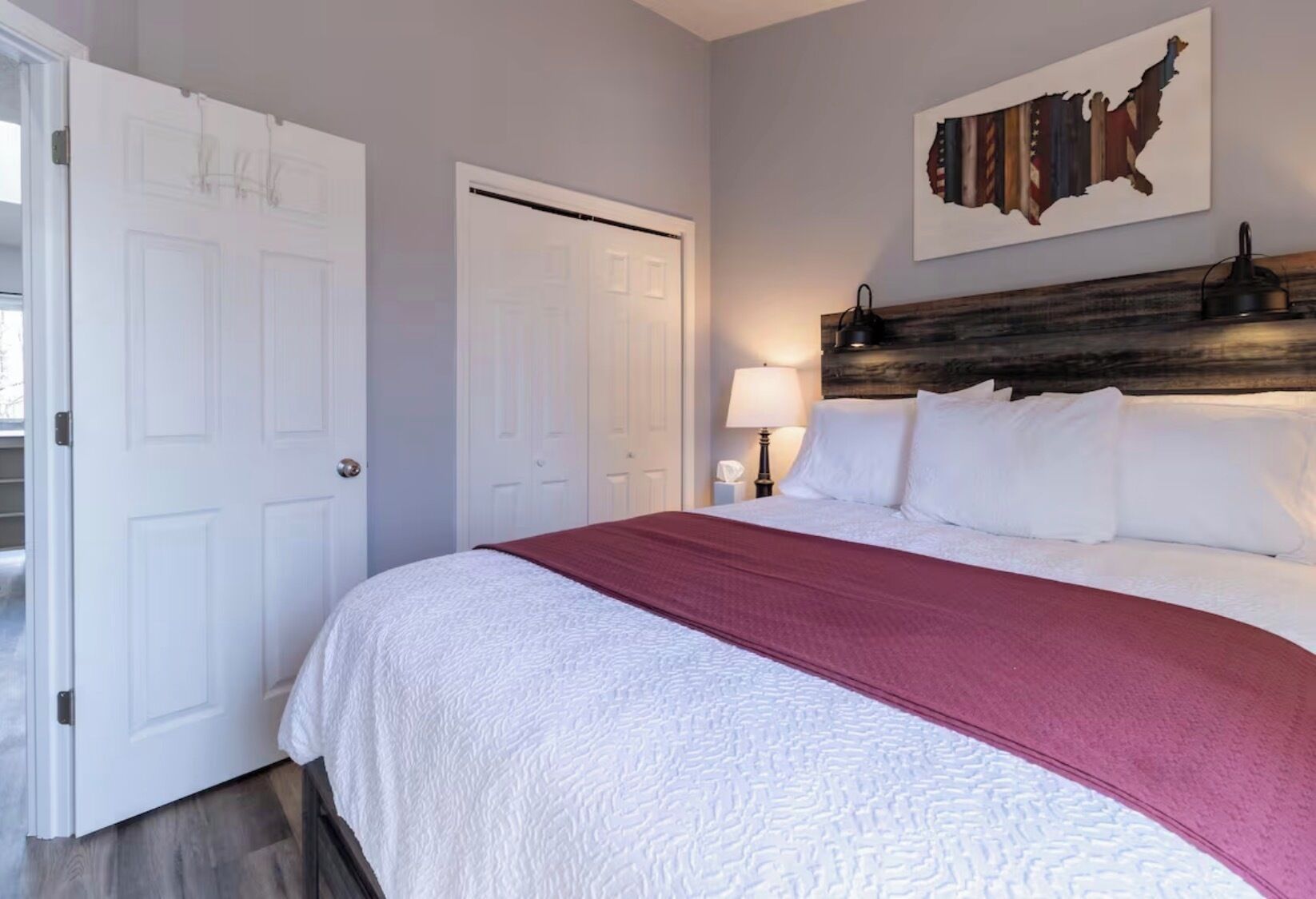 A bedroom with a bed, a headboard, a wall-mounted lamp, and a door.