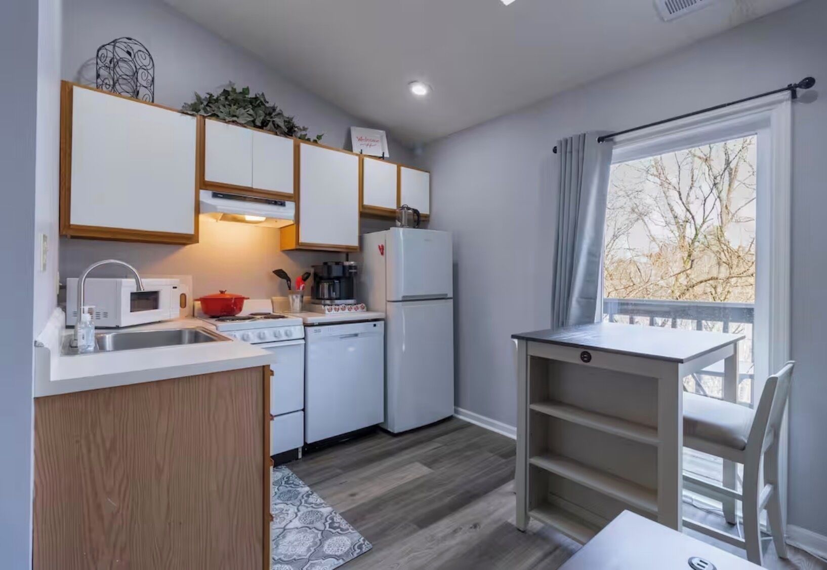 A compact kitchen with white appliances, a wooden cabinet, and a window with a view of trees.