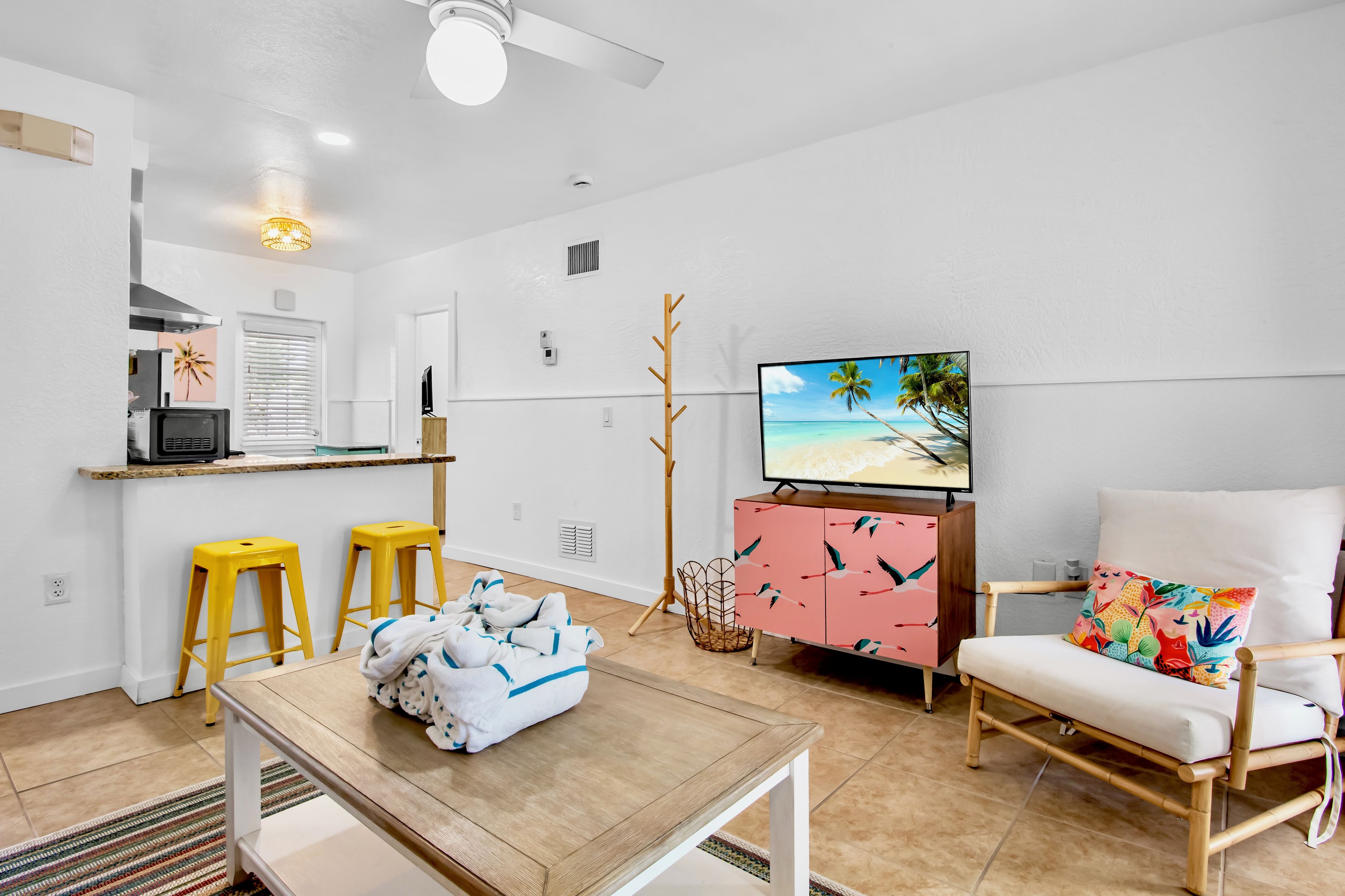 A modern living room with a TV, a wooden coffee table, a chair, and a kitchen area with a fridge and a microwave.