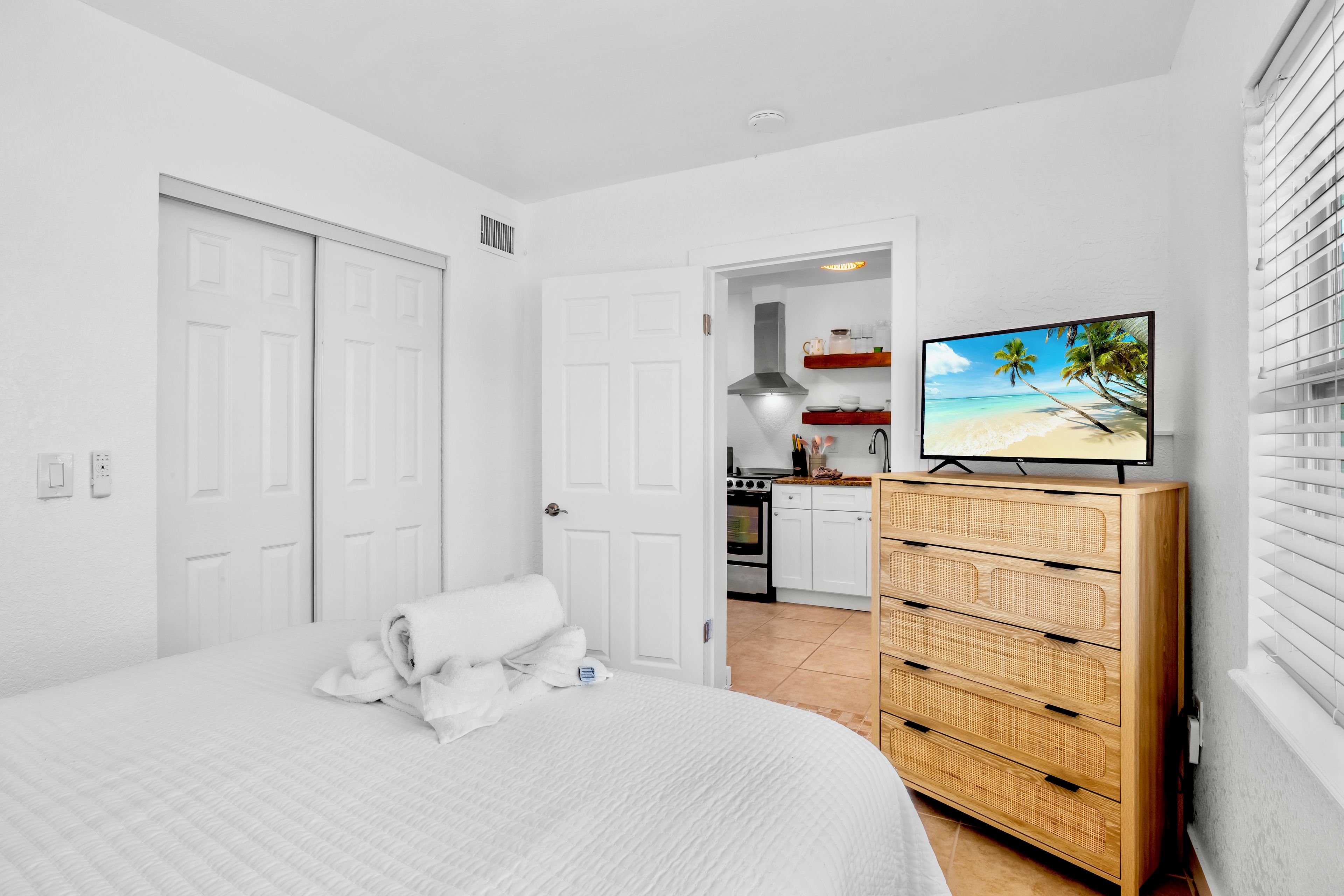 A bedroom with a bed, a wooden dresser, and a television displaying a beach scene.