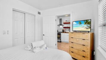 A bedroom with a bed, a wooden dresser, and a television displaying a beach scene.