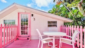 A pink house with a white door, number 3, a small porch, and a white table with chairs. - Sunrise Garden Resort (Anna Maria)