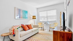 A modern living room with a sofa, a coffee table, a TV, and a painting on the wall. - Sunrise Garden Resort (Anna Maria)