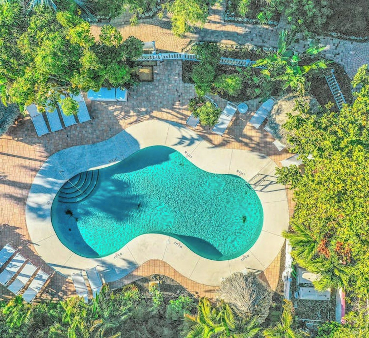 Vista aérea de una piscina rodeada de sillas de descanso y un sendero de piedra.