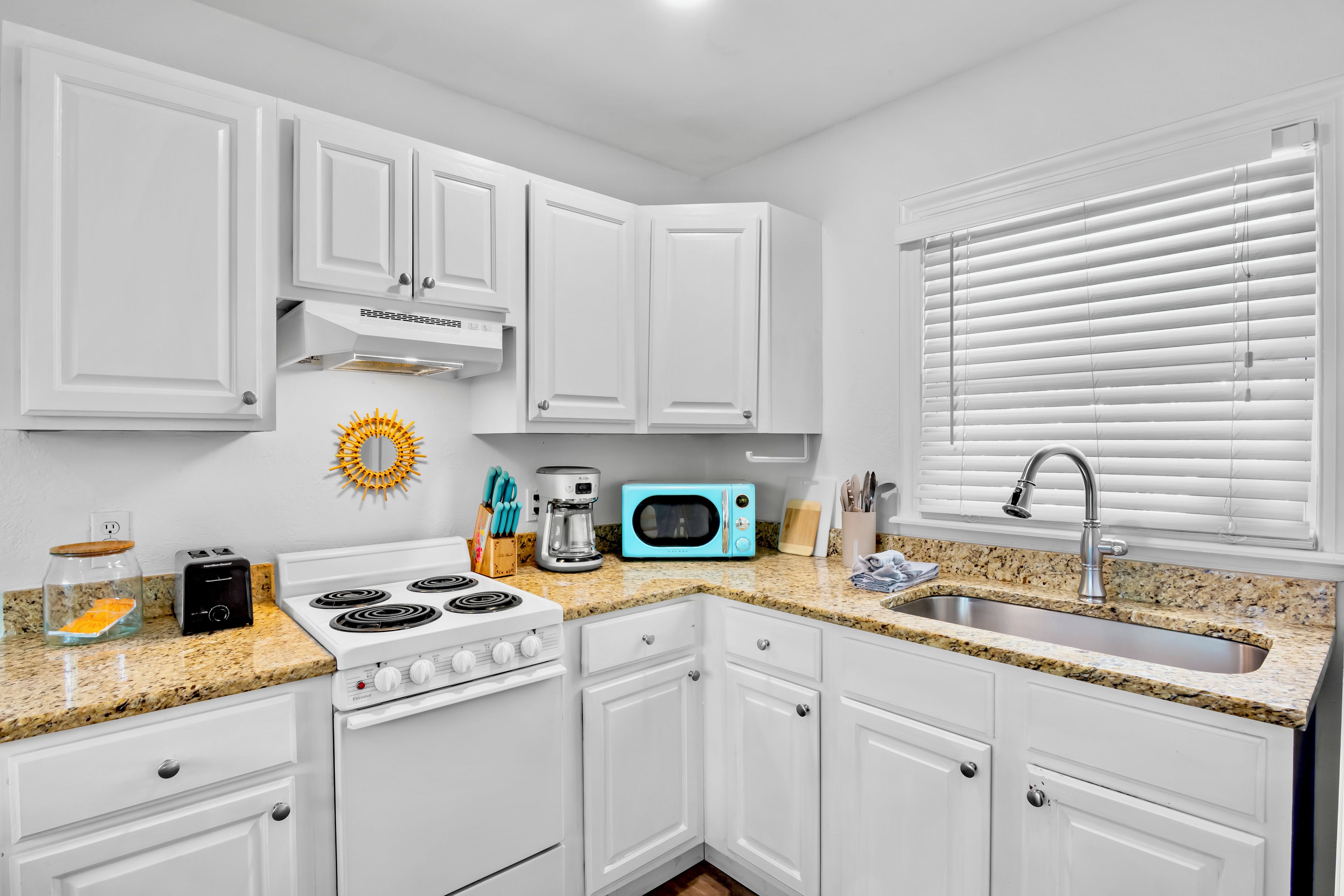 A modern kitchen with white cabinets, a gas stove, a microwave, and a sink.