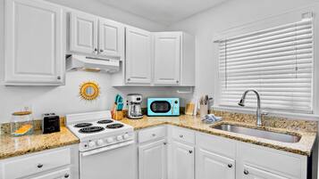 A modern kitchen with white cabinets, a gas stove, a microwave, and a sink.