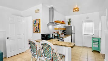 Cocina compacta con una isla central, muebles blancos y una zona de comedor con sillas de colores.