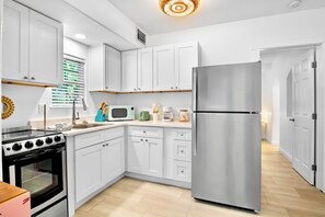 A modern kitchen with white cabinetry, a stainless steel refrigerator, a microwave, and a stove.