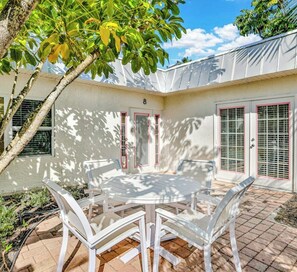 A patio with a round table and chairs, a white door, and a window with blinds.