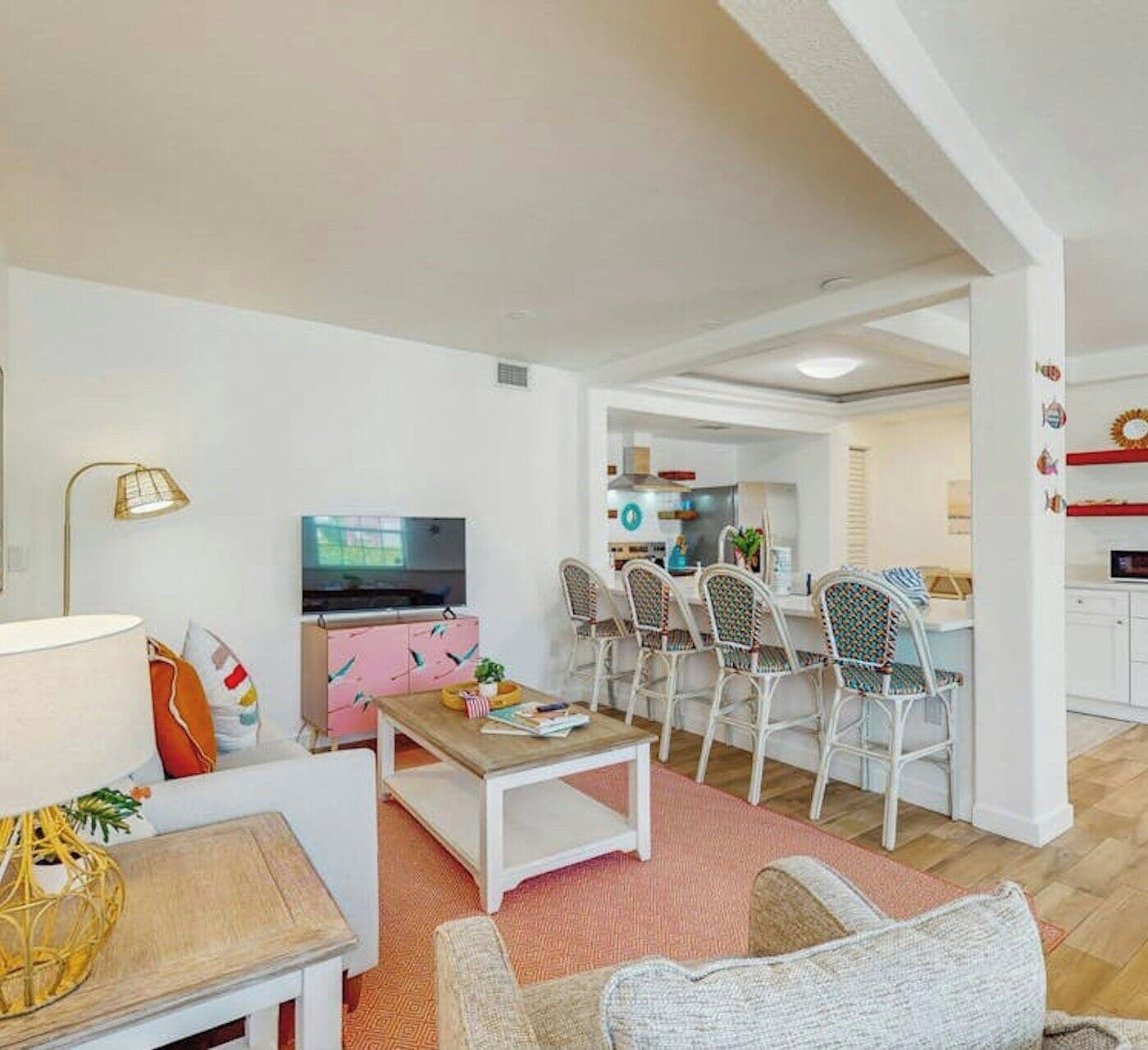Una sala de estar moderna con una televisión, un mueble rosa y una zona de comedor con sillas blancas.