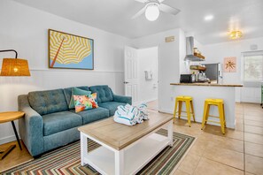 A modern living room with a sofa, a coffee table, and a kitchen area with stools. - Sunrise Garden Resort (Anna Maria)