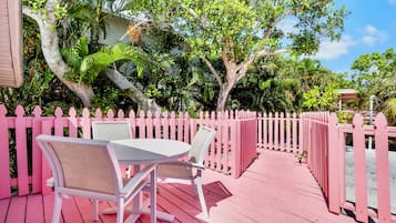 Een roze houten terras met een tafel en stoelen, omringd door een roze hek en weelderige begroeiing.
