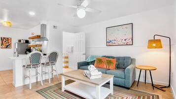 Una sala de estar moderna con sofá, mesa de centro, sillas y un comedor con microondas y refrigerador.