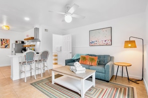 Una sala de estar moderna con sofá, mesa de centro, sillas y un comedor con microondas y refrigerador.
