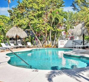 A pool area with lounge chairs, a thatched umbrella, and tropical vegetation.