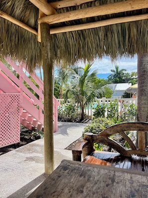 Un espacio al aire libre cubierto con una mesa de madera, techo de paja y cerca rosa.