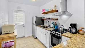 A modern kitchen with white cabinetry, a stainless steel range hood, a built-in oven, and a granite countertop. - Sunrise Garden Resort (Anna Maria)