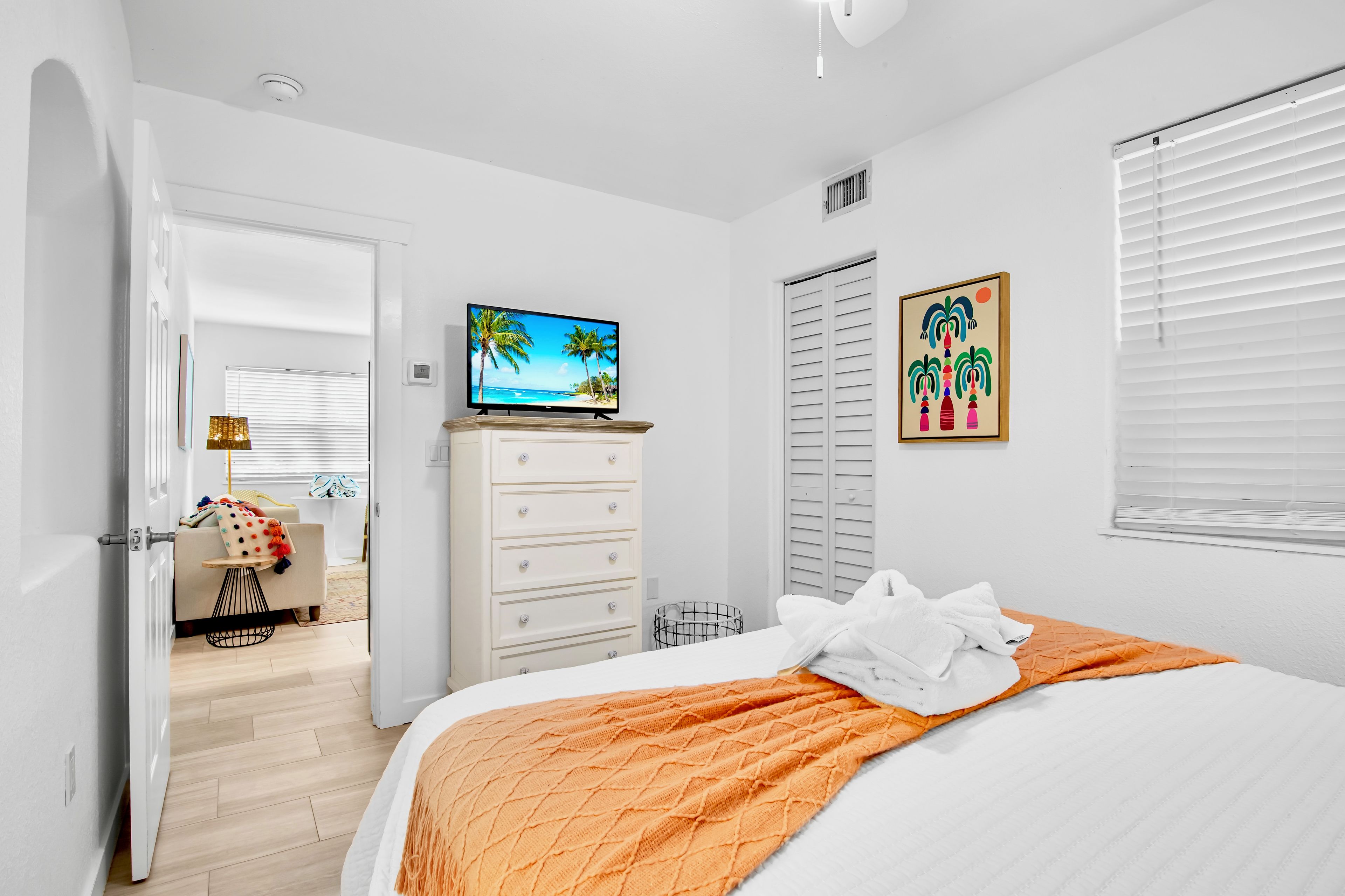 Un dormitorio con cama, televisión, cómoda y puerta que da a otra habitación.