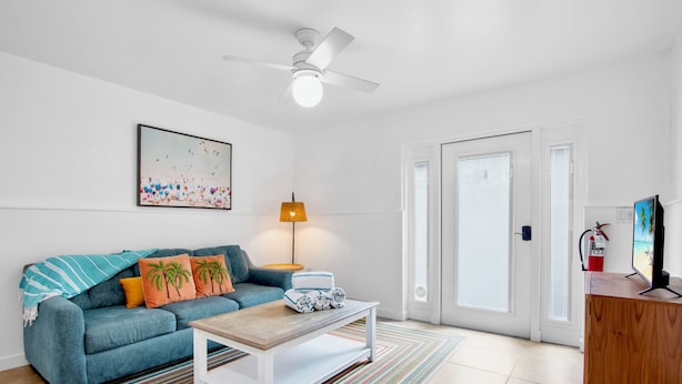 A modern living room with a blue sofa, a coffee table, a painting, a lamp, and a television. - Sunrise Garden Resort (Anna Maria)