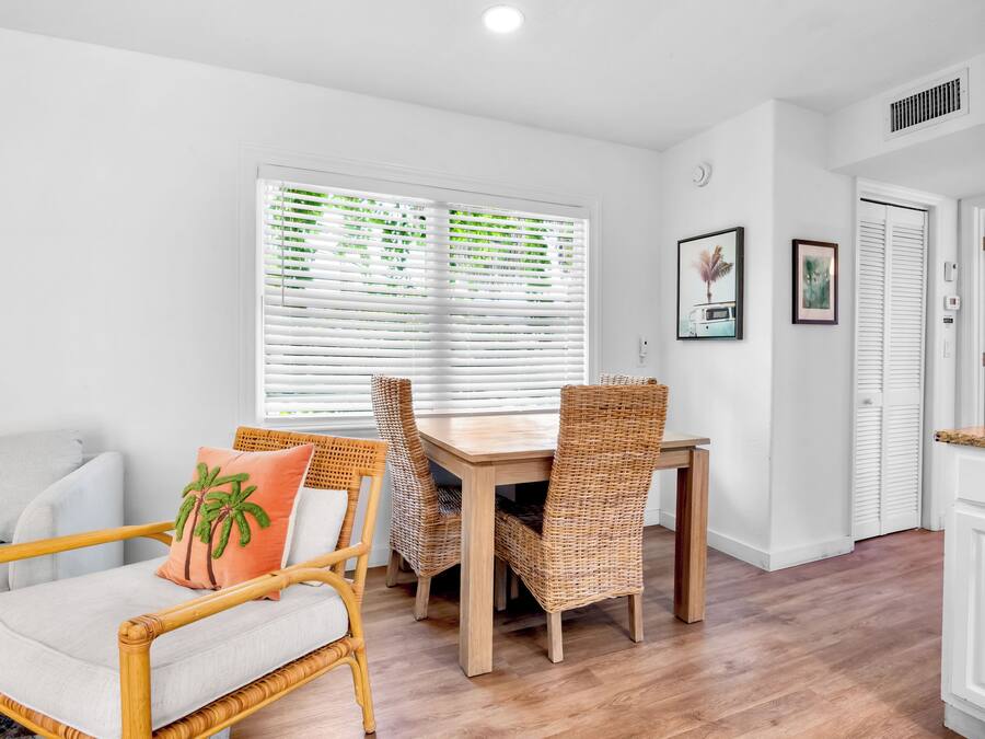 A room with a dining table, chairs, a sofa, and a window with blinds.