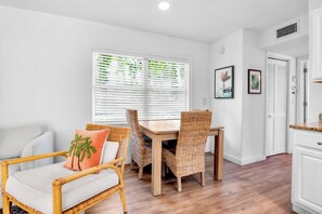 A room with a dining table, chairs, a sofa, and a window with blinds.