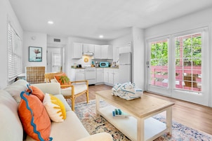 A modern living room with a sofa, a coffee table, and a kitchen area with white cabinets and appliances.
